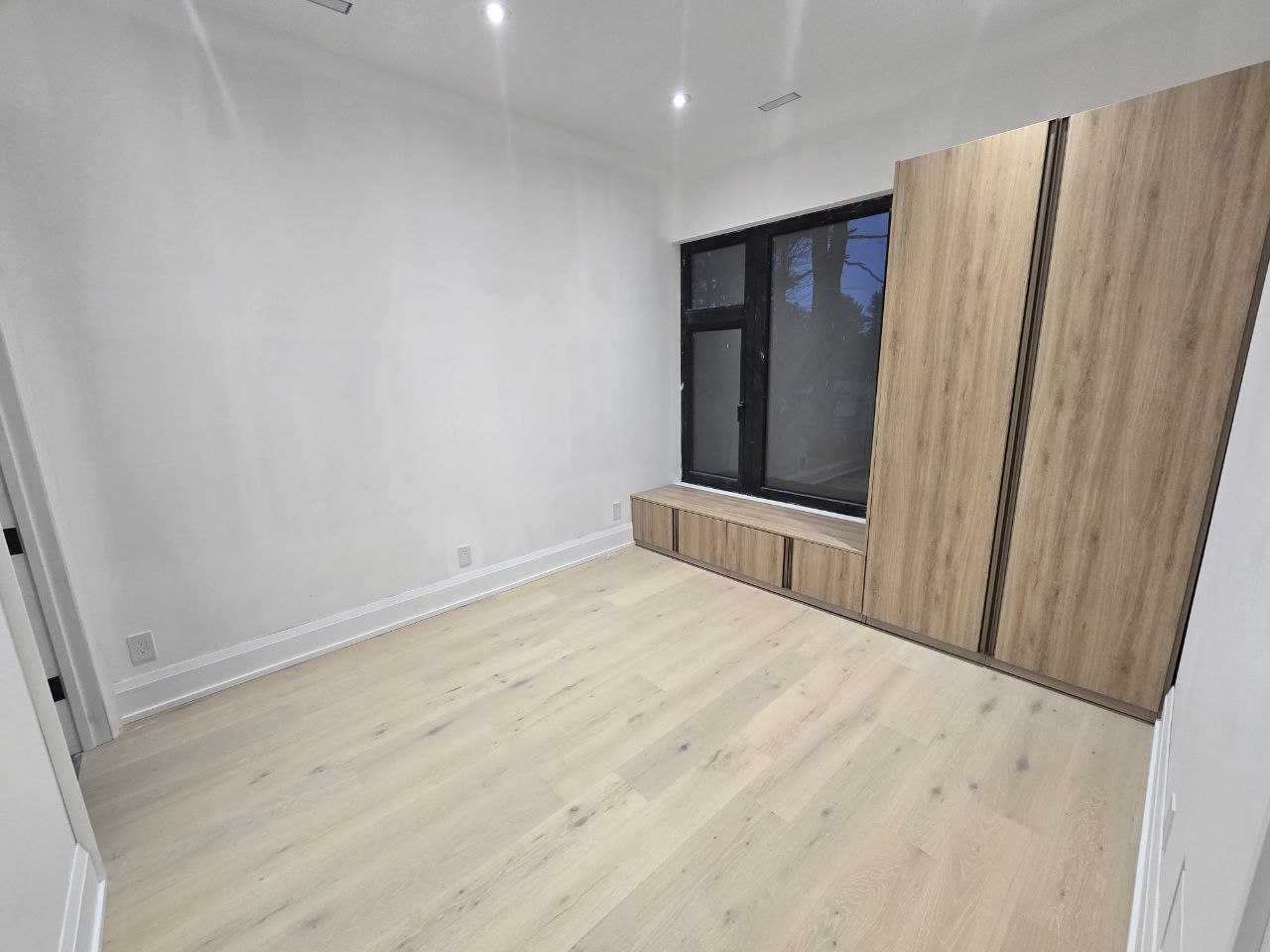 View of the second bedroom, featuring hardwood floors and a large window providing natural light